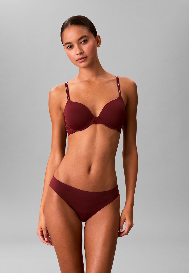 Burgunderfarbener Push-up-BH mit Spitzenakzenten und verstellbaren Trägern, kombiniert mit passenden Bikinislips aus glattem Stoff.