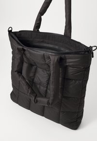 Borsa tote imbottita nera con due manici, dotata di chiusura superiore con zip e texture a rombi. L'interno è foderato in un tessuto liscio.