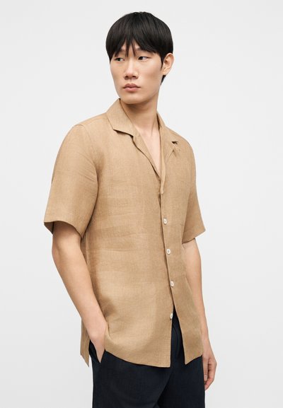 Πουκάμισο με κοντά μανίκια και κουμπιά, σε ανοιχτό καφέ υφασμα με υφή. Διαθέτει γιακά με άνοιγμα και λευκά κουμπιά, συνδυασμένο με μπλε παντελόνι.