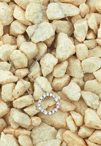 Collana in argento con un pendente circolare di gemme trasparenti poggiato su pietre beige grezze.