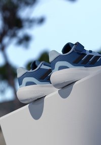 Sinised spordijalatsid võrgust üliskihi, kontrastsete mustade triipude ja valge tallaga. Varustatud pehme krae ja takjakinnitusega rihmaga.