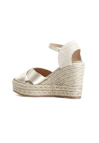 Sandalias de cuña metálicas doradas con diseño de correas cruzadas, suela de yute trenzado y talón abierto con acentos de tela texturizada.