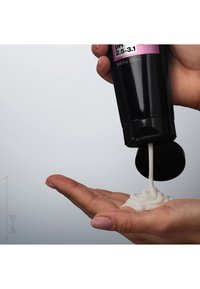 Bouteille squeeze noire dispersant une crème épaisse et blanche dans une paume ; le récipient est doté d'un capuchon flip et d'une étiquette avec pH 2.5-3.1, volume de 250 ml.