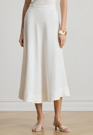 Valge midi-seelik kerge kangaga, millel on voogav siluett ja peenääris, kombineeritud läbipaistvate kontsadega sandaalidega.