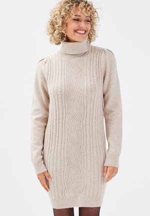 Abito maglione beige lavorato a maglia con colletto alto, caratterizzato da motivi a treccia, maniche lunghe e polsini a coste. Texture morbida, lunghezza a metà coscia.