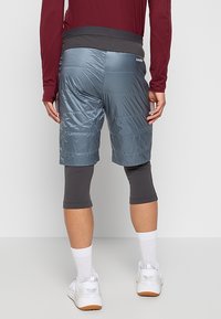 Herrarnas träningsshorts, grå med kviltad textur, kombinerat med åtsittande mörka tights, vita strumpor och sportskor, sett bakifrån.