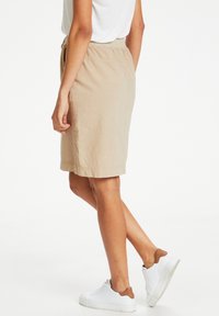 Jupe beige jusqu'aux genoux en tissu texturé avec une taille élastique, associée à des baskets blanches, illustrant un look décontracté.
