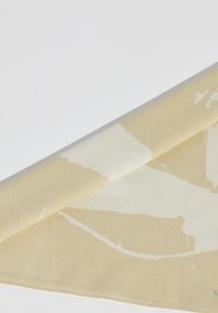 Tela beige con un gran patrón abstracto color crema, doblada con una textura suave y un dobladillo cosido a lo largo del borde.