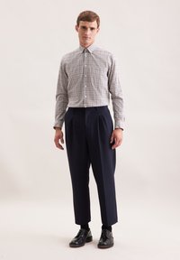 Geverfde button-up shirt in beige en bruin, gecombineerd met marineblauwe geplooide broek en zwarte veterschoenen, wat een nette uitstraling creëert.