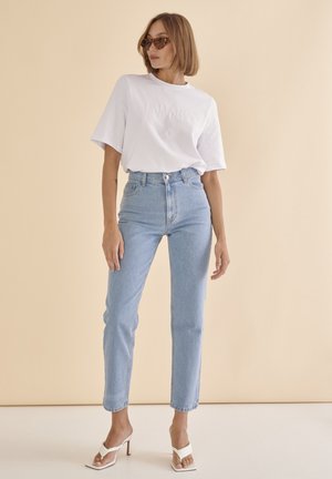 Tricou alb din bumbac, cu text embosat, asortat cu blugi deschiși la culoare, cu talie înaltă și sandale albe cu toc, având o croială lejeră.