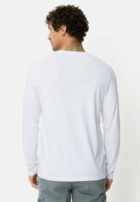 Wit overhemd met lange mouwen van zachte stof, met een eenvoudig ontwerp met een ronde hals en geribbelde manchetten, gezien van achteren.