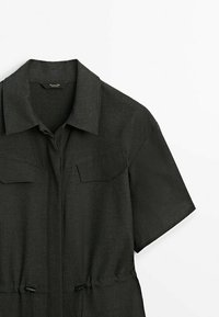 Dark gray short-sleeve jumpsuit with a collared neck, two chest pockets, drawstring waist, and smooth textured fabric.