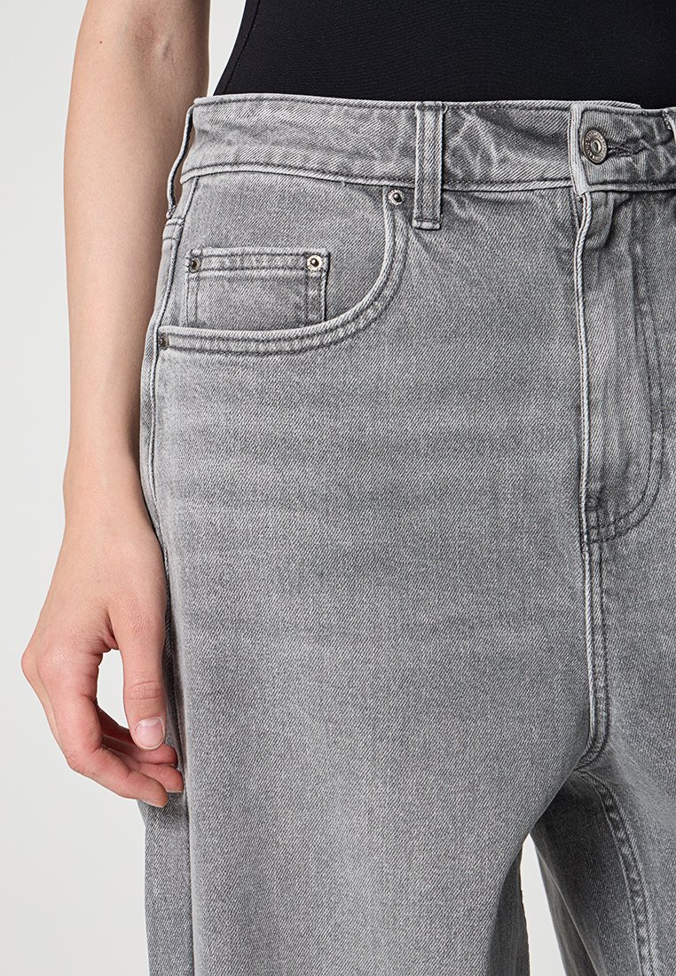Jeans in denim grigio con vita alta, design classico a cinque tasche, leggere sfumature e cuciture tonali. Inquadratura ravvicinata della parte anteriore.