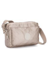 Beige nylon crossbody bag with a front pocket, logo patch, silver hardware, and a decorative charm. Features an adjustable strap.