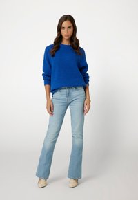 Niebieski sweter dziergany o strukturalnym wykończeniu, zestawiony z jasnoniebieskimi dżinsami w dzwony oraz beżowymi szpilkami o szpiczastym nosku. Prosty, codzienny strój.