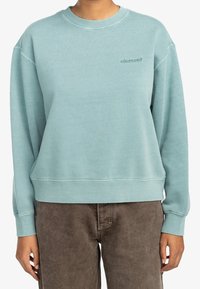 Sweat-shirt bleu clair avec col rond, poignets et ourlet côtelés. Il présente un petit logo brodé sur la poitrine et une coupe décontractée.