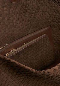 Brown woven fabric interior of a bag, featuring a brown leather zippered pocket with gold hardware and smooth texture.