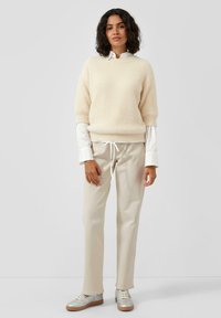 Jasne beżowe sweter z teksturą, z krótkimi rękawami, nałożony na bia�łą koszulę. Kremowe spodnie i srebrne sneakersy dopełniają stylizację.