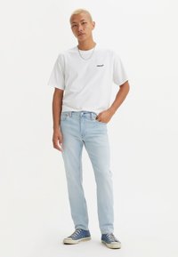 Witte T-shirt met korte mouwen en zwart logo, lichte blauwe jeans en blauwe sneakers. Eenvoudig ontwerp, casual pasvorm met denimtextuur.