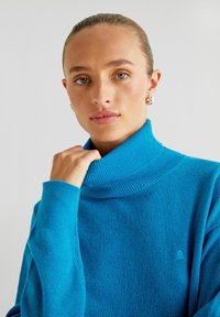 TÜRQUOISE Rollkragenpullover aus weichem Material, mit geripptem Kragen und Bündchen, und einem dezenten Logo-Detail auf der Brust.