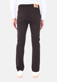 Pantaloni in denim marrone con vestibilità dritta, caratterizzati da un'etichetta in pelle sulla cintola posteriore e due tasche posteriori. Indossati con sneakers bianche.