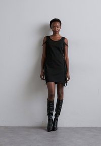 Fekete, ujjatlan ruha nyitott vállrésszel, sima textúrával és oldalra kötött részletekkel. Térd fölé érő fekete csizmával párosítva. Minimalista dizájn.