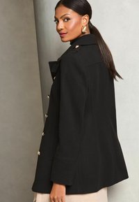 Cappotto in misto lana nero con design strutturato, dettagli in bottone dorato e colletto appuntito. Tessuto morbido con vestibilità su misura.