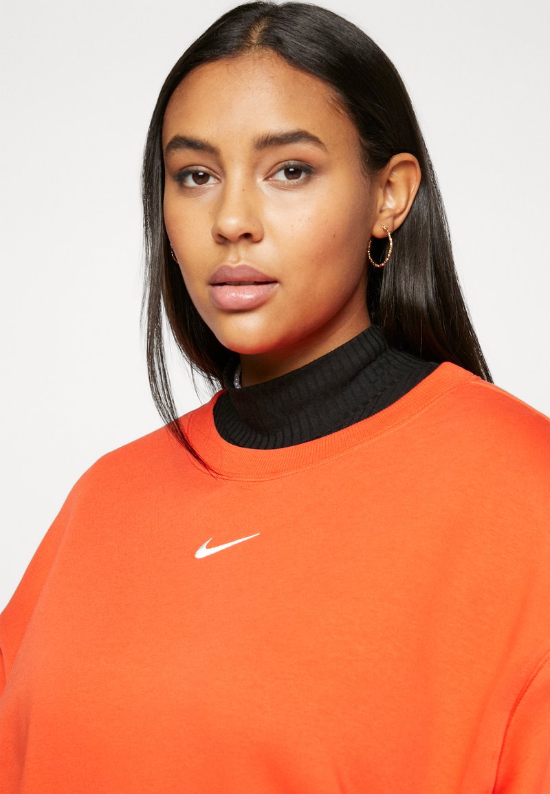 Sweatshirt orange à col rond, présentant un col roulé noir à côtes en dessous et un petit logo blanc de Nike sur la poitrine.
