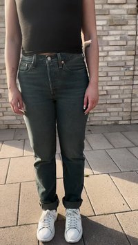 Tamnozelene traperice visokog struka s ravnim nogavicama, koje imaju zatvaranje na gumbe sprijeda i uvijene manžete, u kombinaciji s bijelim tenisicama.