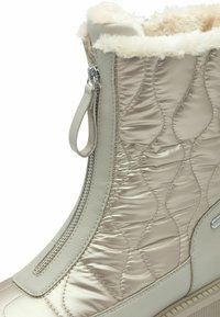 Botte imperméable beige avec textile matelassé et cuir, doublure en fausse fourrure, fermetures éclair sur le côté et semelle en caoutchouc nervurée.