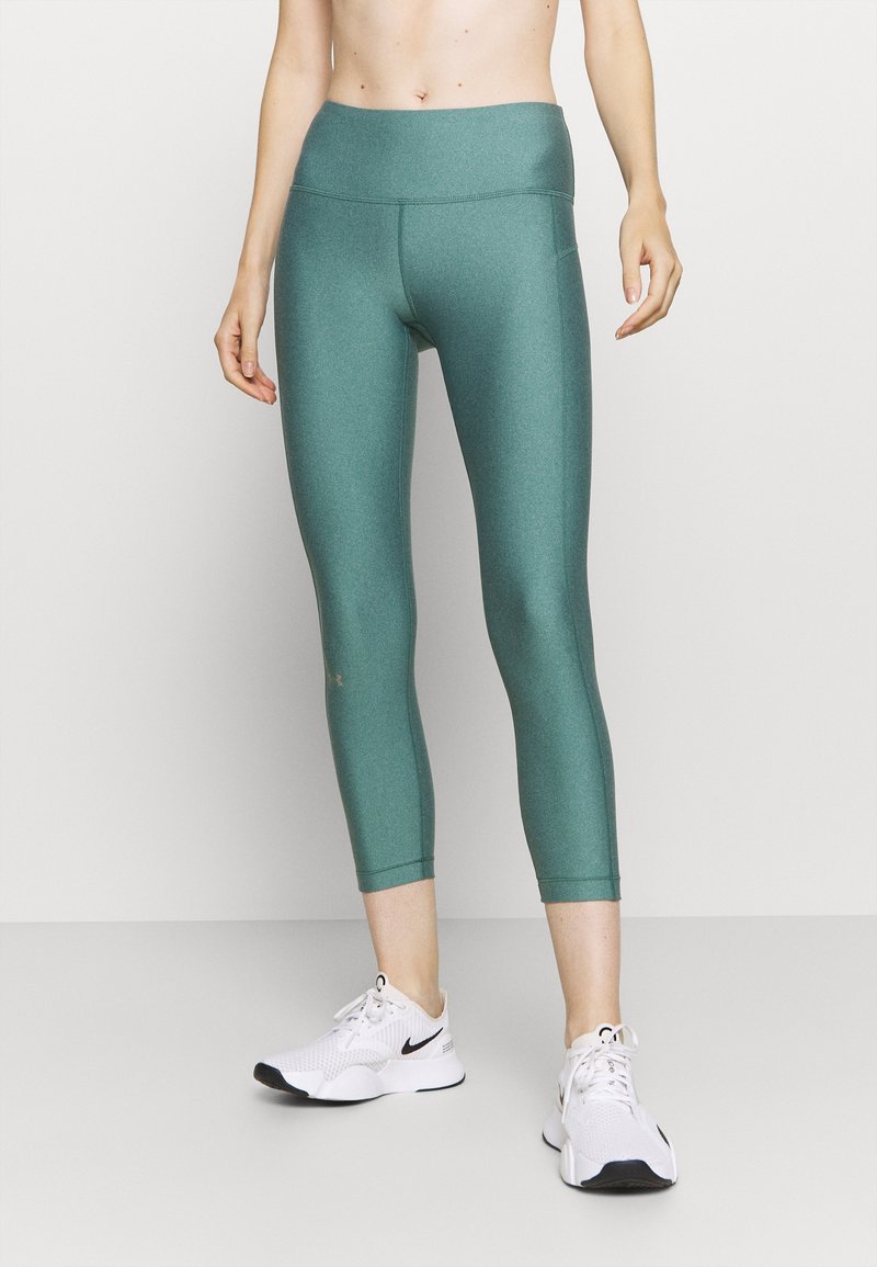 Teal, wysokie legginsy capri wykonane z elastycznego materiału; gładka tekstura z płaskimi szwami. W zestawie z białymi butami sportowymi.