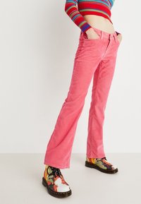 Pantalones de pana rosa acampanados con bolsillos frontales, combinados con botas de patrón multicolor que tienen cordones y una suela gruesa.
