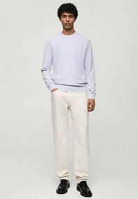 Pulover cu guler rotund de culoare violet deschis asortat cu pantaloni de un alb murdar. Modelul poartă pantofi negri, evidențiind un material moale și o croială lejeră.