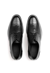 Schwarze Leder-derbyschuhe mit Brogue-Details, runder Spitze und Schnürdesign. Glatte Textur mit perforierten Akzenten an der Schuhspitze.