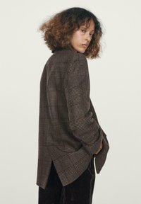 Blazer a quadri marrone con vestibilità rilassata, dotato di colletto a punte, maniche lunghe e orlo spaccato. Tessuto strutturato con una finitura morbida.