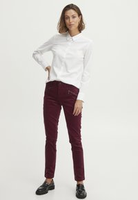 Biela košeľa na gombíky a bordové slim-fit nohavice s vreckami na zips, v kombinácii s čiernymi mokasínami. Hladká textúra látky, strih na mieru.