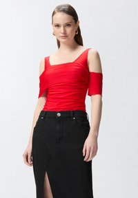Top rojo ajustado con mangas cortas y escote cuadrado, combinado con una falda de mezclilla negra de talle alto con una abertura frontal.