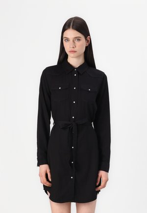 Robe noire à manches longues, avec un boutonnière sur le devant, deux poches poitrine et une ceinture nouée à la taille. Tissu doux, design minimaliste et fentes sur les côtés.