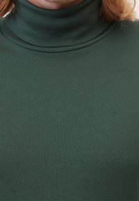 Musta vihreä pooloneule, jossa on kiinteä siluetti ja joka on valmistettu sileästä, joustavasta kankaasta. Ominaisuuksiin kuuluu korkea kaulus ja saumatonta muotoilua.