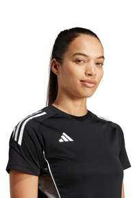 Maglietta sportiva nera a maniche corte, con strisce bianche sulle spalle e un logo sul petto. Presenta un design aderente e una texture liscia.