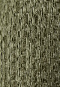 Textured fabric in olive green featuring raised, wavy patterns with a soft sheen. The surface exhibits a distinct, rippled texture.