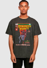 Black oversized t-shirt featuring a graphic print of a monster and text from "Stranger Things," with a distressed texture and round neckline.
