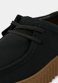 Sorte snørebukser med glatt matte overflate, rund tå, detaljert søm og en beige gummisåle med vertikale riller.