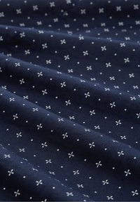 Marinblått tyg med vitt blommönster och prickar, strukturerad yta, vikt med synliga veck, med små dekorativa detaljer.