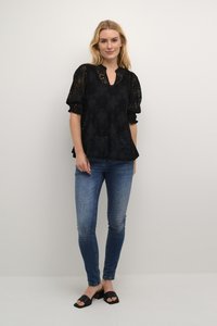 Črna čipkasta bluzica z obsežnimi kratkimi rokavi, dekorativnim cvetličnim vzorcem in v-izrezom. Kombinirana z oprijetimi modrimi kavbojkami in črnimi natikači.