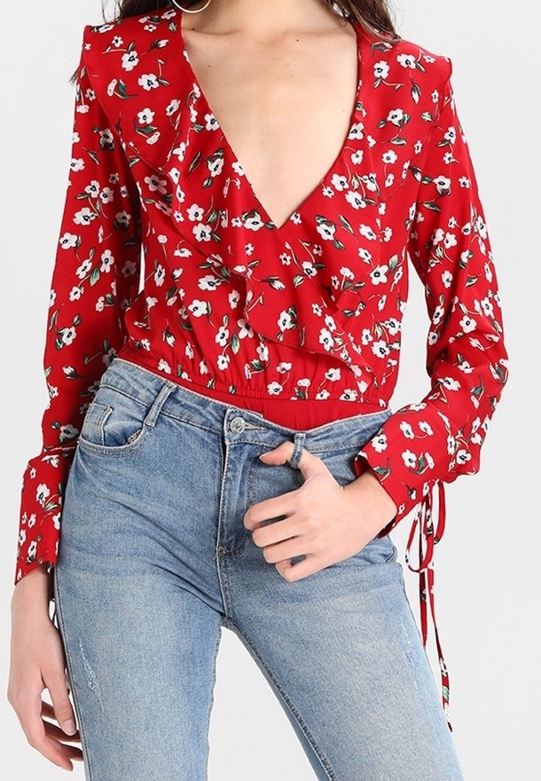 Blusa roja de flores de manga larga con un escote en V profundo, parte delantera con volantes y cintura ajustada, combinada con jeans de tiro alto en azul claro.