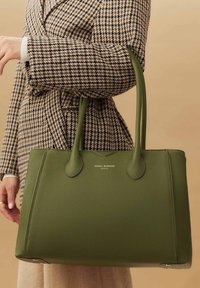 Grüne Leder-Umhängetasche mit strukturierter Oberfläche, ausgestattet mit zwei geschwungenen Griffen und dezentem Logo-Detailing auf der Vorderseite.