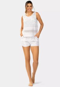 Biała bezrękawnik o teksturowanym wzorze, w połączeniu z dopasowanymi, białymi szortami z falbankowym wykończeniem i kieszeniami. Lekkie materiały.