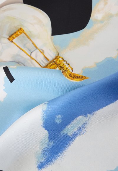 Gros plan sur un tissu avec une ampoule imprimée, ciel bleu, nuages blancs et une partie d'un chapeau noir ou d'un objet.