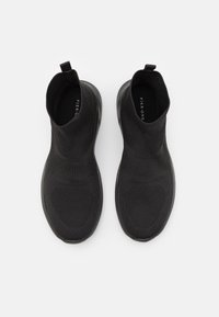 Czarne sneakersy wsuwane z dzianinową cholewką, elastycznym kołnierzem i teksturowaną podeszwą. Minimalistyczny design, z gładkim wykończeniem i bez widocznego logo.